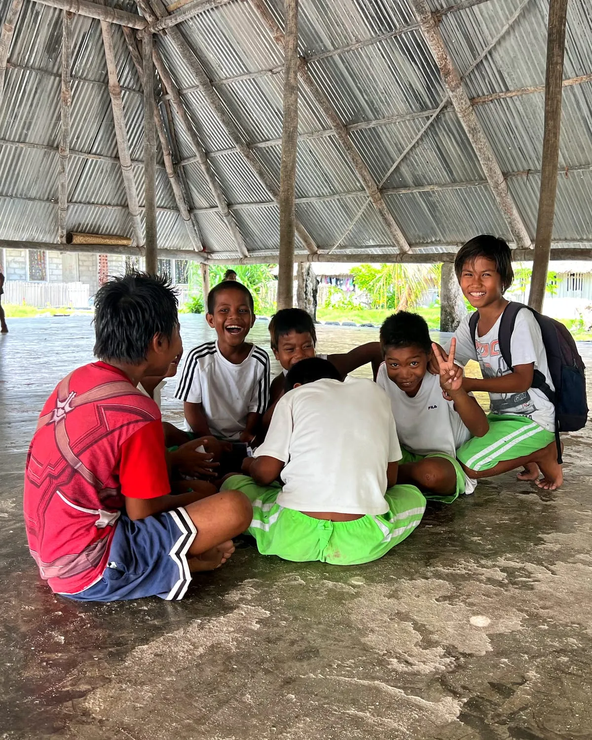 Children laughing together in a game under the roof of a maneaba in Kiribati